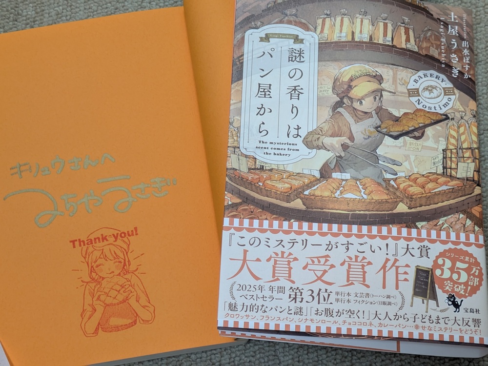 土屋うさぎ先生のサイン入り『謎の香りはパン屋から』(宝島社/このミステリーがすごい!大賞受賞作)。オレンジ色の見返しに金色インクで「キリュウさんへ」のメッセージとサイン、メロンパンを抱える女の子のスタンプ付き。