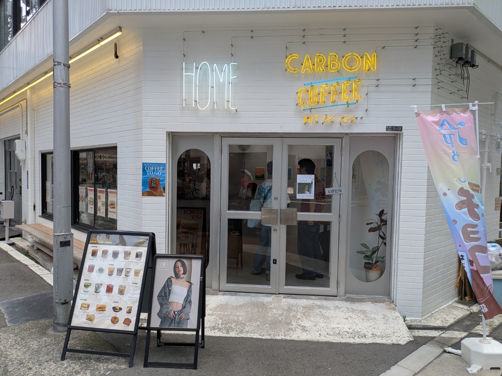 "CARBON COFFEE OSAKAの外観、HOMEとCARBON COFFEEのネオンサインが目印の白い店舗"