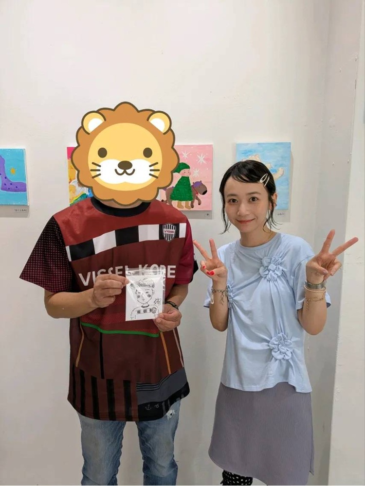 "似顔絵屋さんイベントで三戸なつめさんと記念撮影、完成した似顔絵を手にピースサイン"
