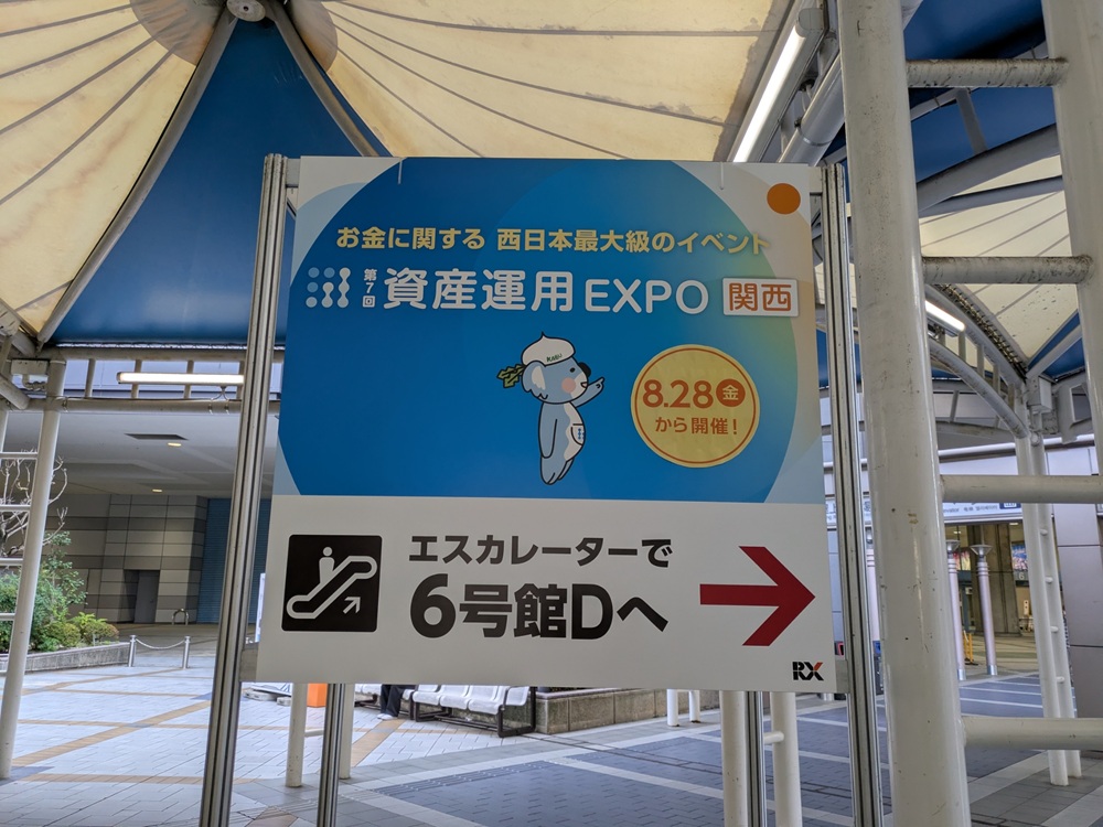 「エスカレーターで6号館Dへ」と書かれた資産運用EXPO関西の会場内案内サイン